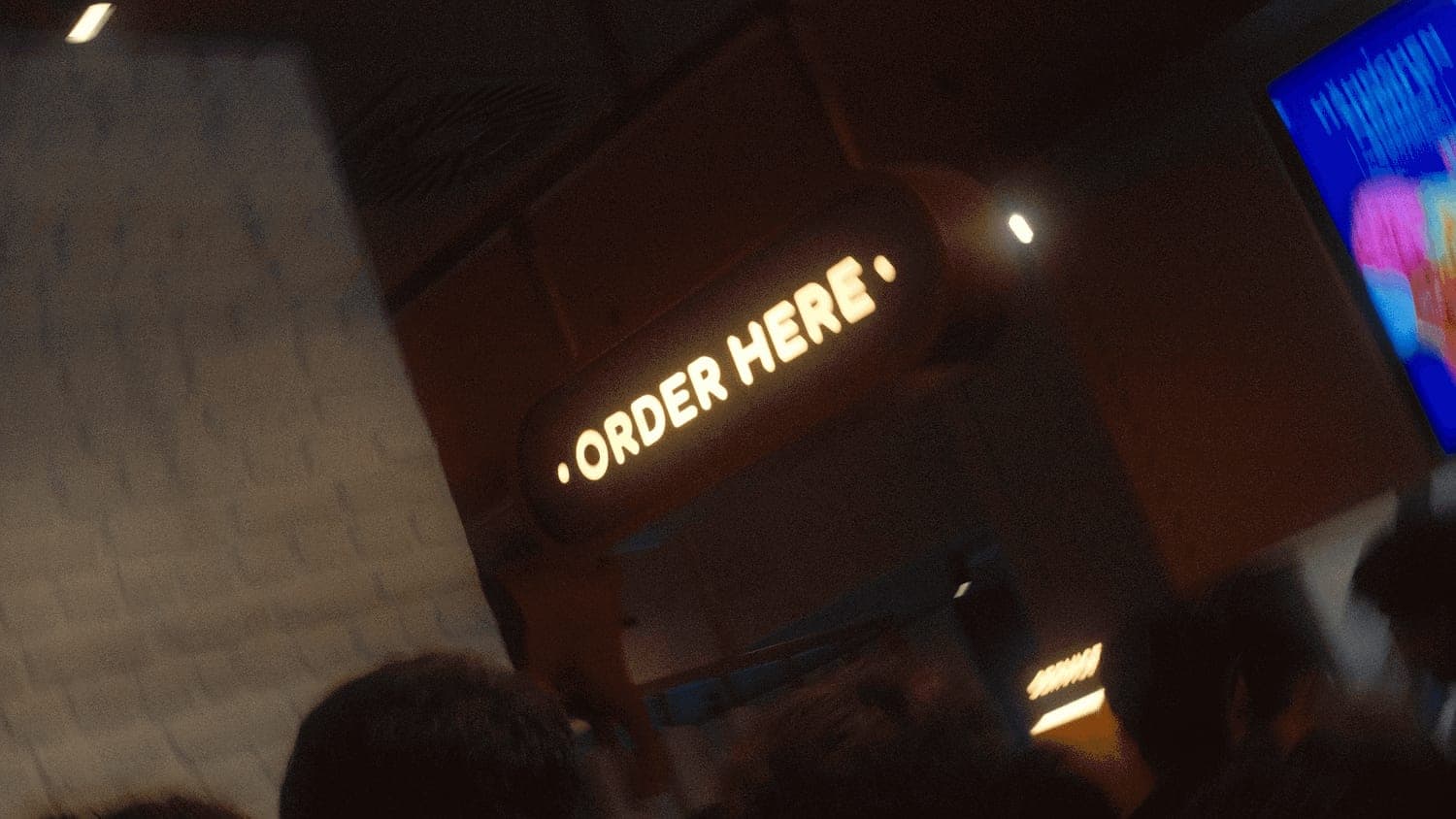 Leuchtschild „Order here“ über der Theke im Kölner Store, davor wartende Gäste