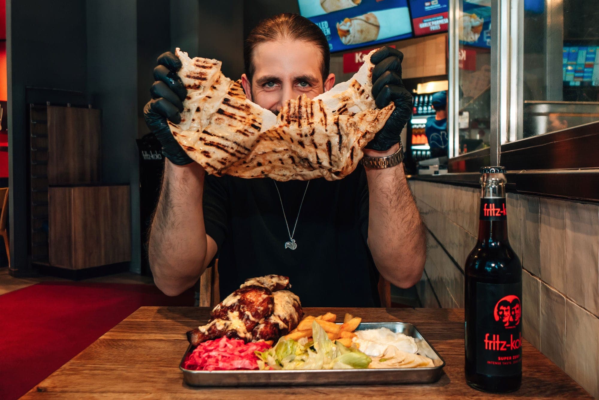 Gast beißt in frisch gegrilltes Spezialbrot, davor ein Tablett mit Hähnchen Spezial im Store