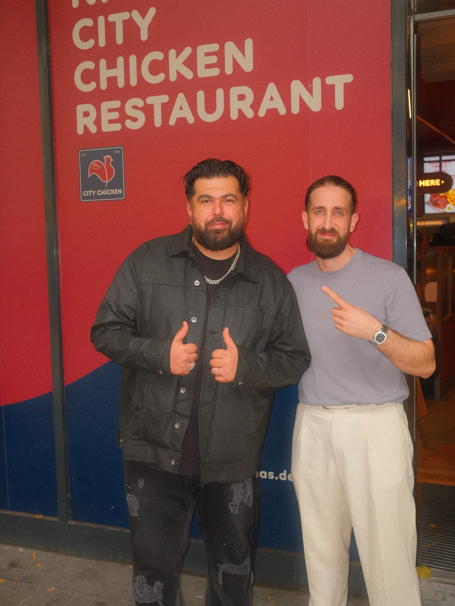 Rapper Summer Cem und Omar Nhas vor der Fassade des Kölner Stores mit dem Schriftzug City Chicken Restaurant